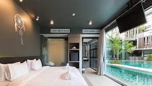 A modern hotel room with a large bed, a view of an infinity pool, and a dreamcatcher on the wall.