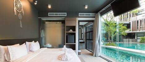 Una habitación de hotel moderna con una cama grande, vistas a una piscina infinita y un atrapasueños en la pared.