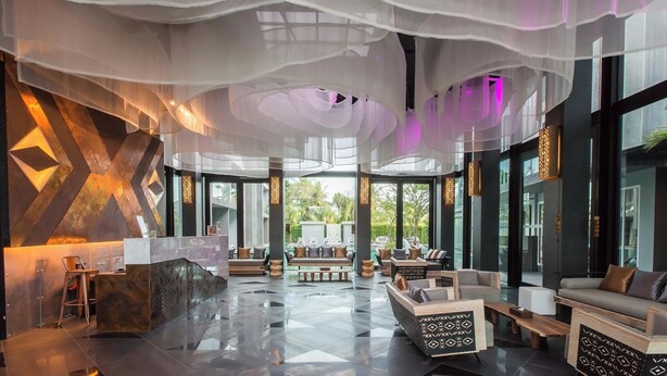 A spacious lobby with a modern design, featuring a reception desk, seating areas, and large windows offering views of the outdoors.