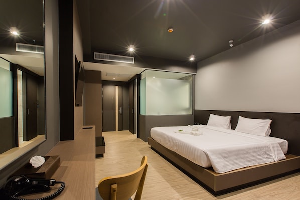 Habitación de hotel moderna con una cama grande, un escritorio y una silla. Hay un espejo en una pared y una ventana en la otra.