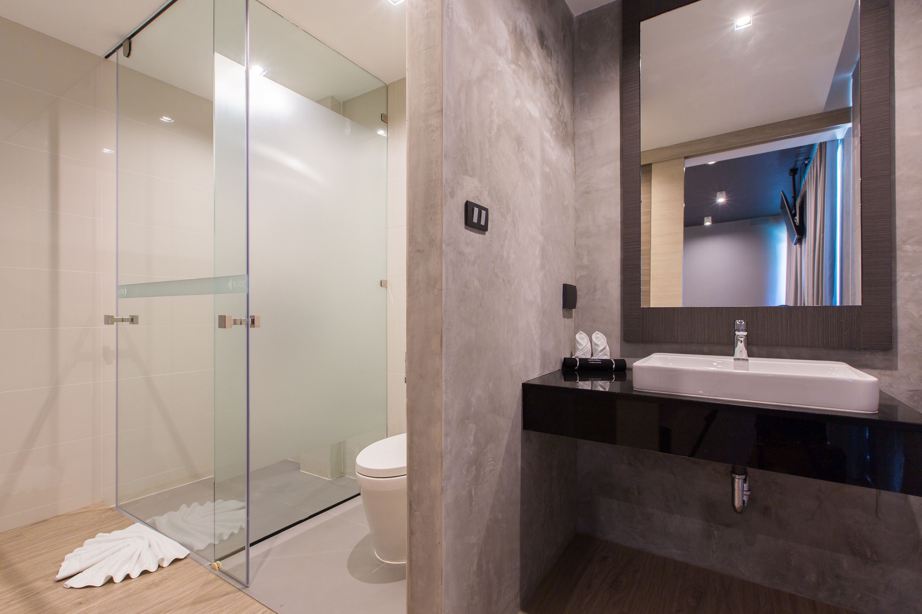 A modern bathroom with a glass shower enclosure, a white toilet, and a black sink with a mirror above it.