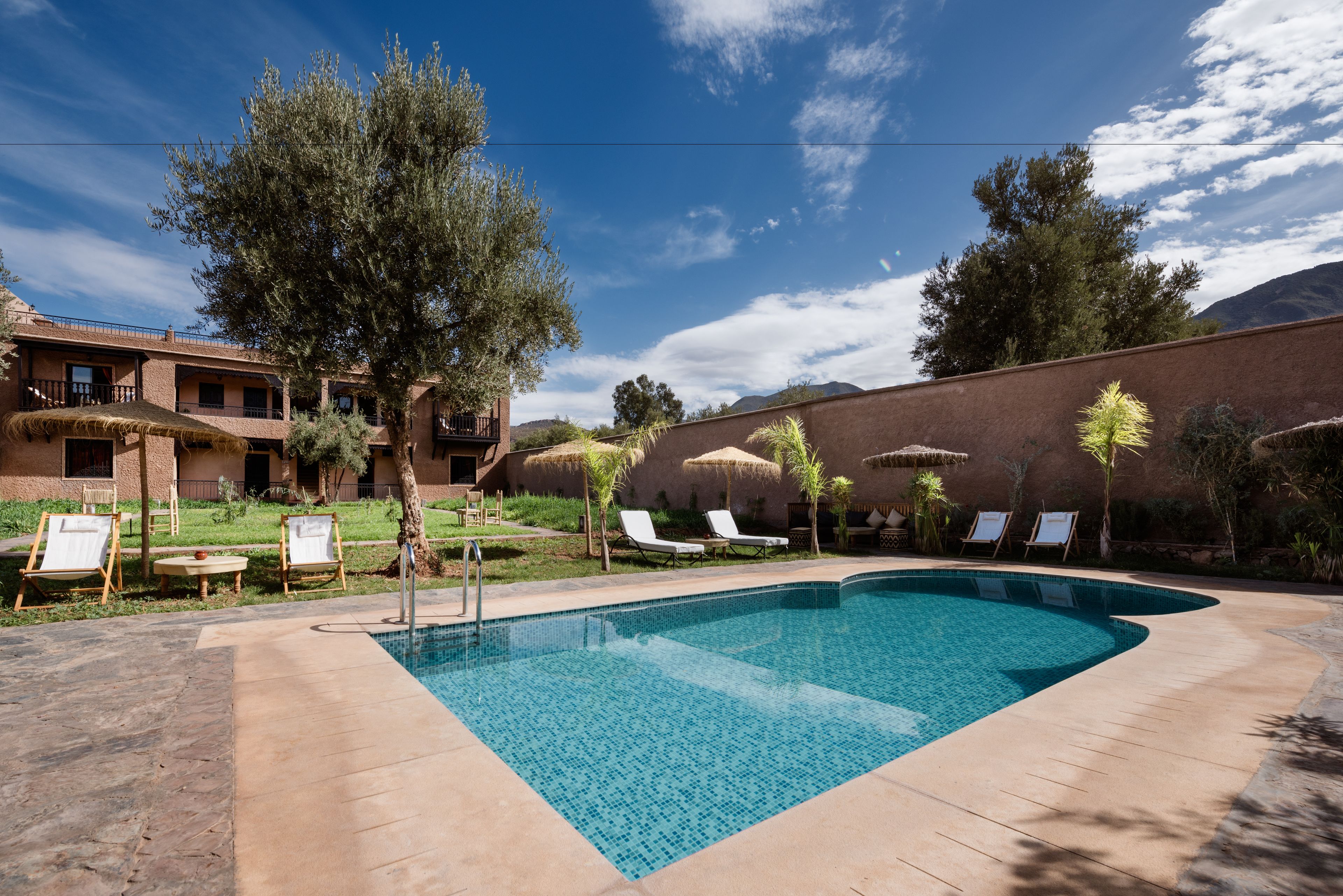 Una piscina con sillas de descanso, una estructura de techo de paja y un edificio con fachada de ladrillo.