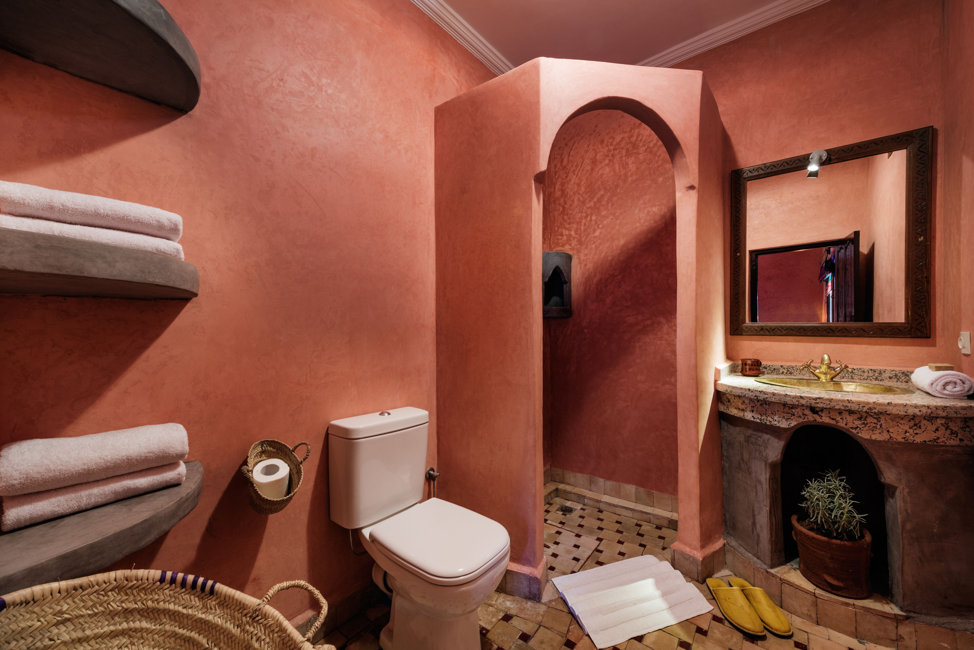 Een badkamer met toilet, wastafel, spiegel, handdoeken, een mand en slippers.