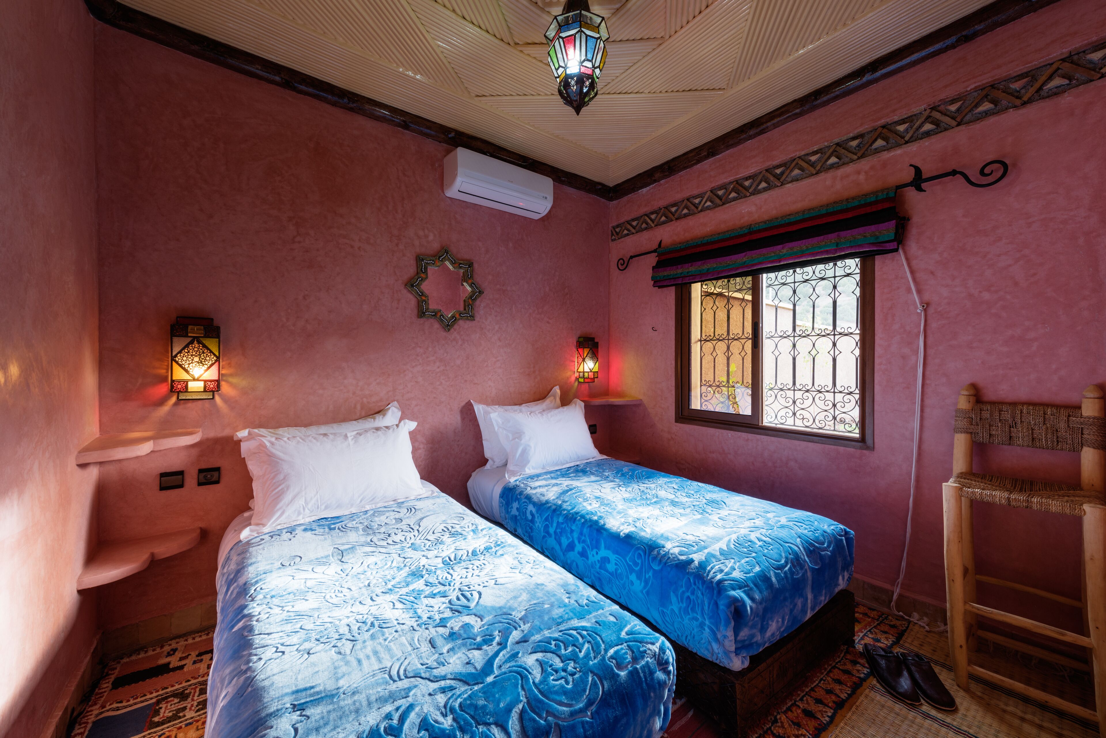 A room with two beds, a hanging chair, a window with bars, and decorative wall lights.