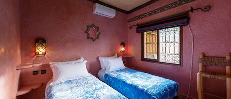 A room with two beds, a hanging chair, a window with bars, and decorative wall lights.