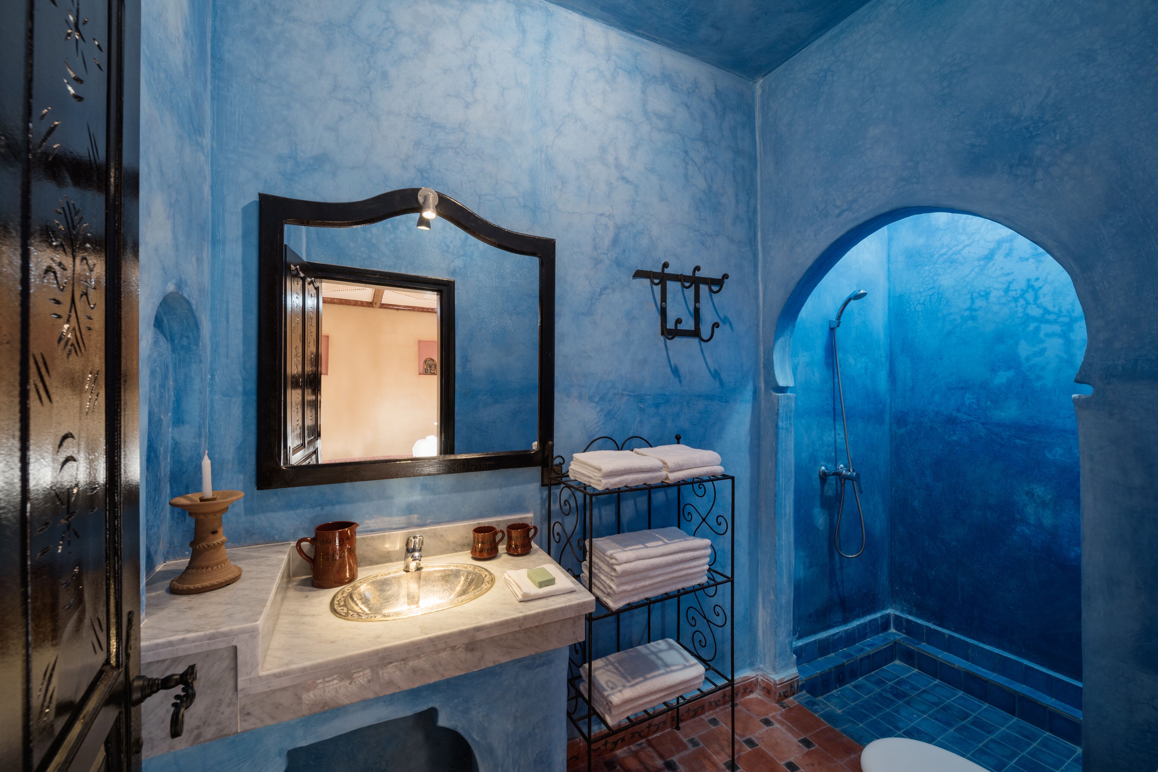 A bathroom with a blue wall, a sink with a mirror, a towel rack, and a shower area.