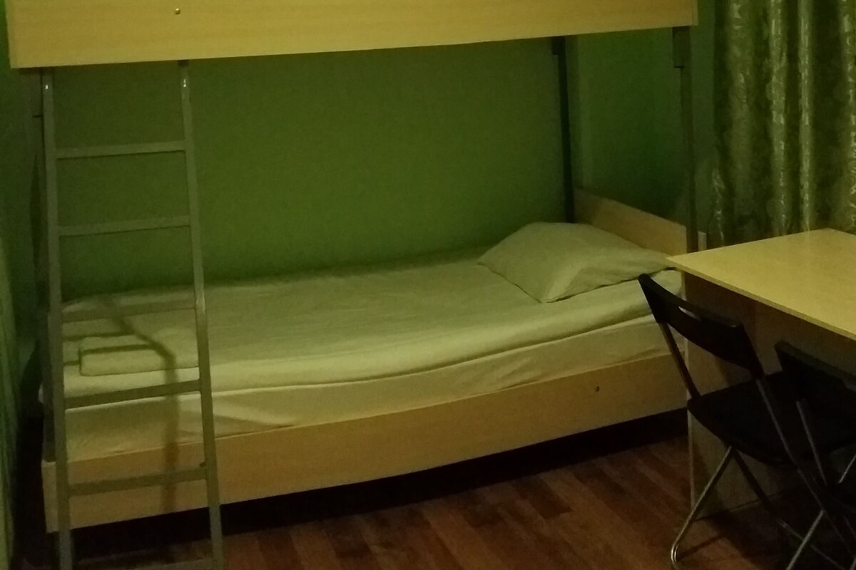 Habitación con literas, escritorio, silla, paredes verdes y suelo de madera.