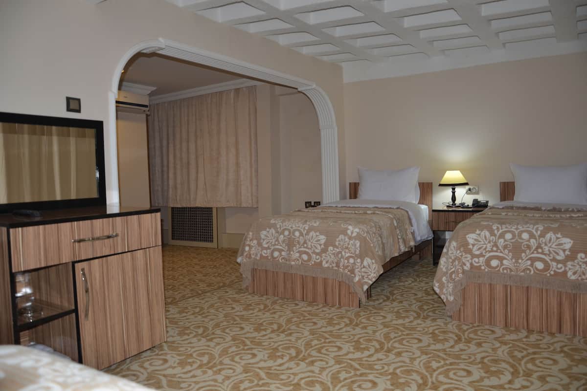 A hotel room with two beds, a wardrobe, a mirror, a lamp, and a ceiling with a grid pattern.