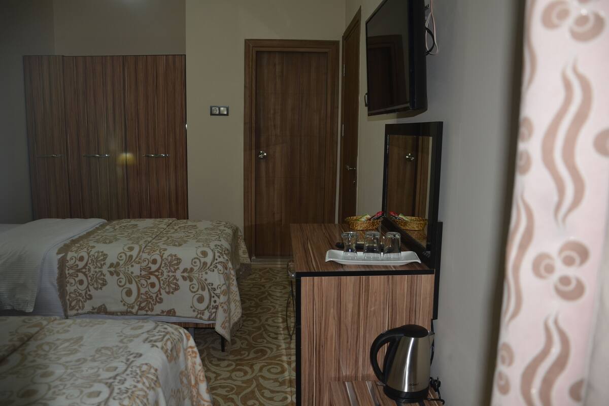 A hotel room with two beds, a wooden wardrobe, a desk with a mirror, and a television on the wall.