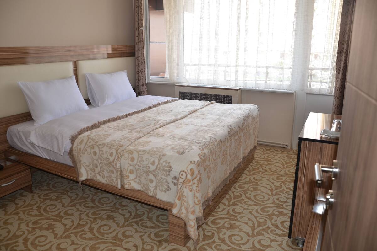 A hotel room with a bed, a dresser, a window with curtains, and a patterned carpet.