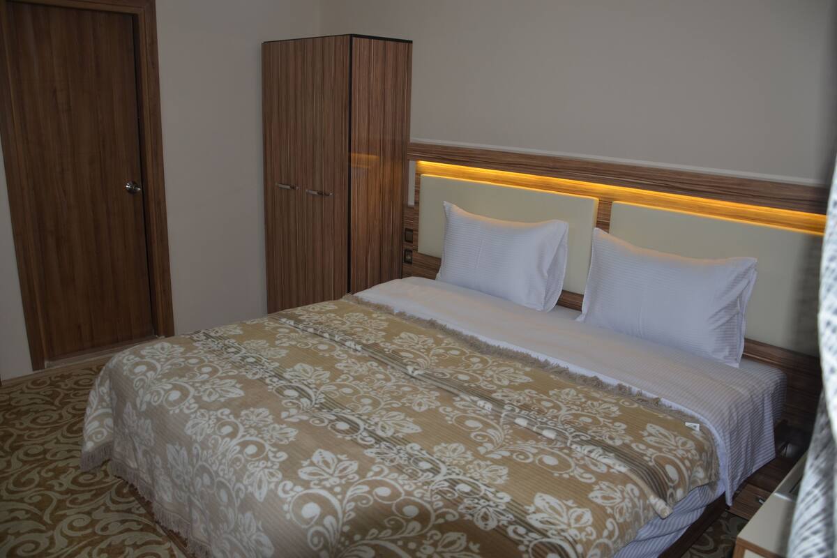 A hotel room with a large bed, a wardrobe, and a headboard with built-in lighting.