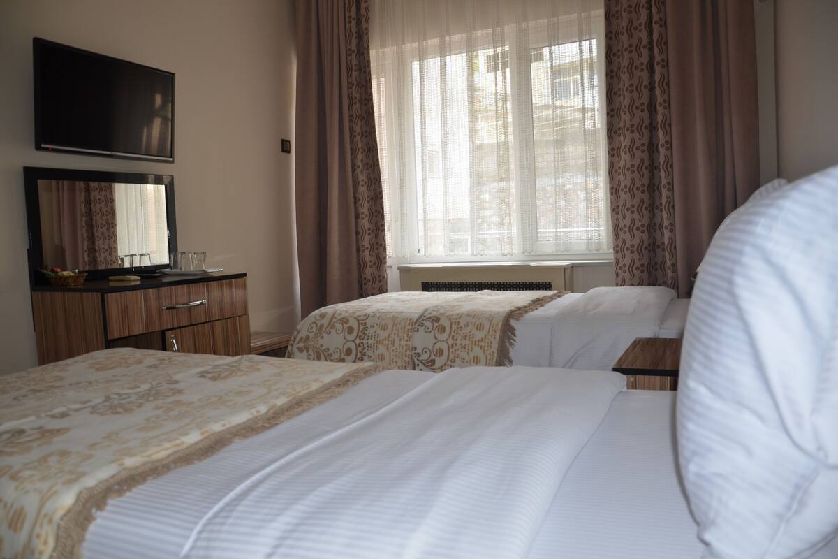 A hotel room with two beds, a TV, a dresser, and a window with curtains.