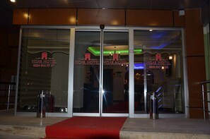 L’entrée de l’hôtel Hisar est marquée par un tapis rouge qui mène aux portes, lesquelles sont agrémentées d’une enseigne lumineuse.