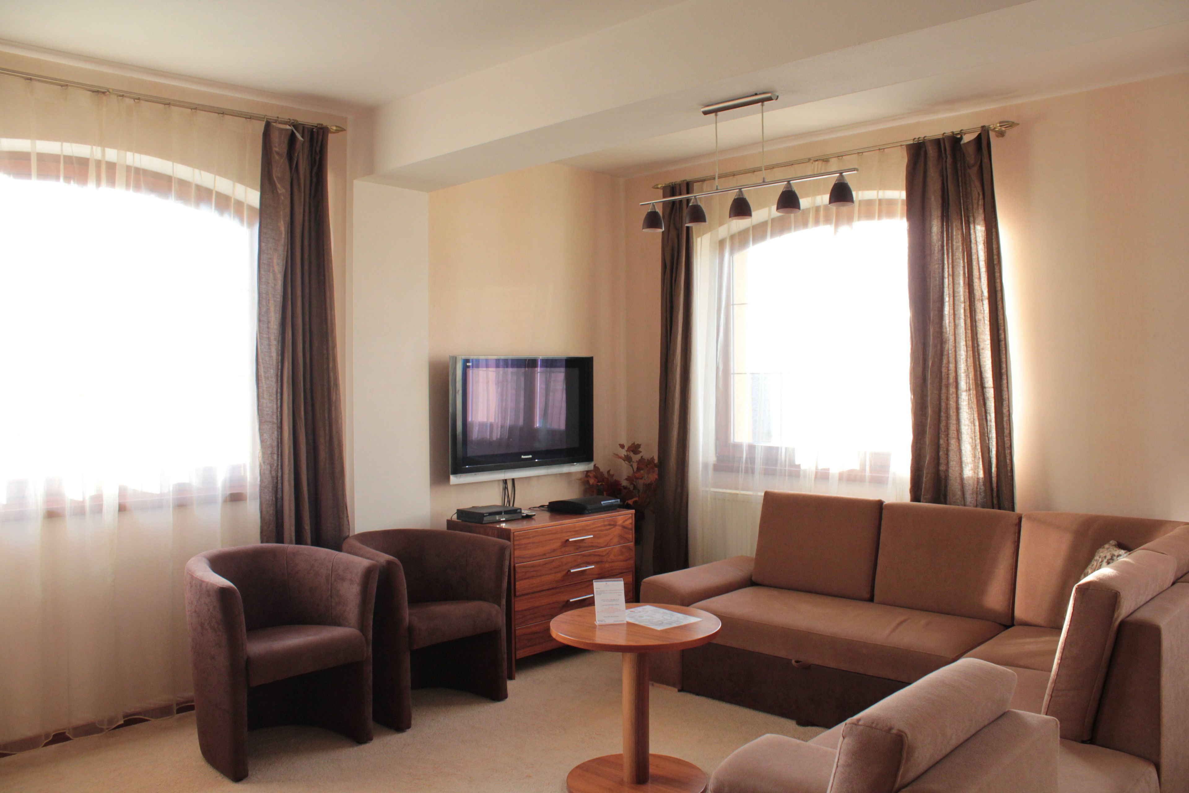 Una habitación de hotel moderna con un sofá grande, dos sillones, una mesita de madera y un televisor de pantalla plana.
