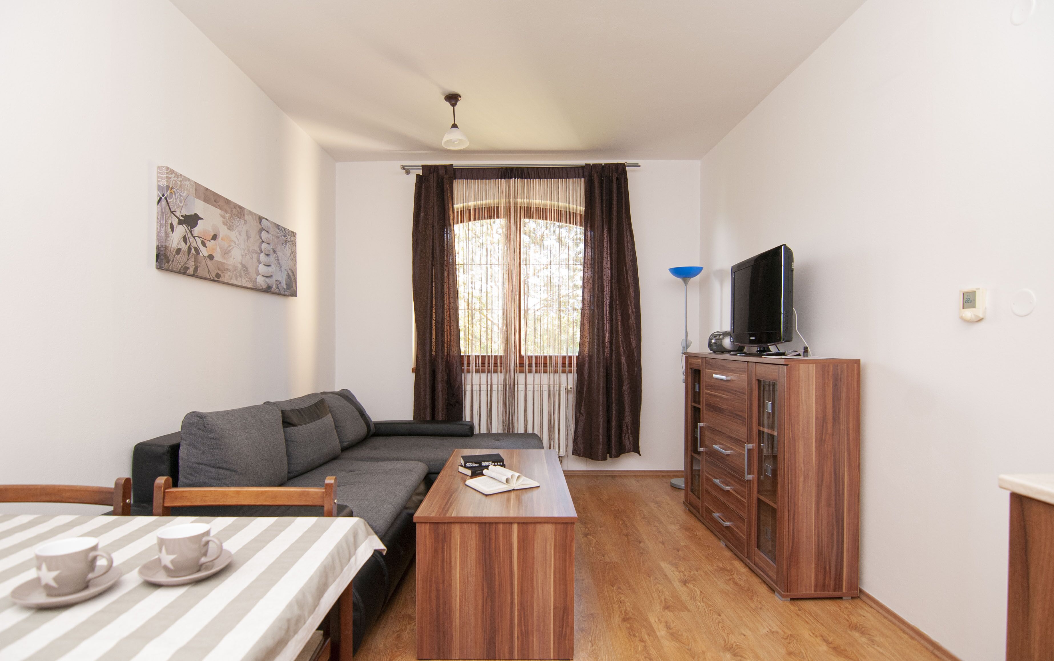 Un salon moderne avec un canapé, un meuble en bois, un téléviseur et un coin repas agrémenté d’une nappe à rayures.