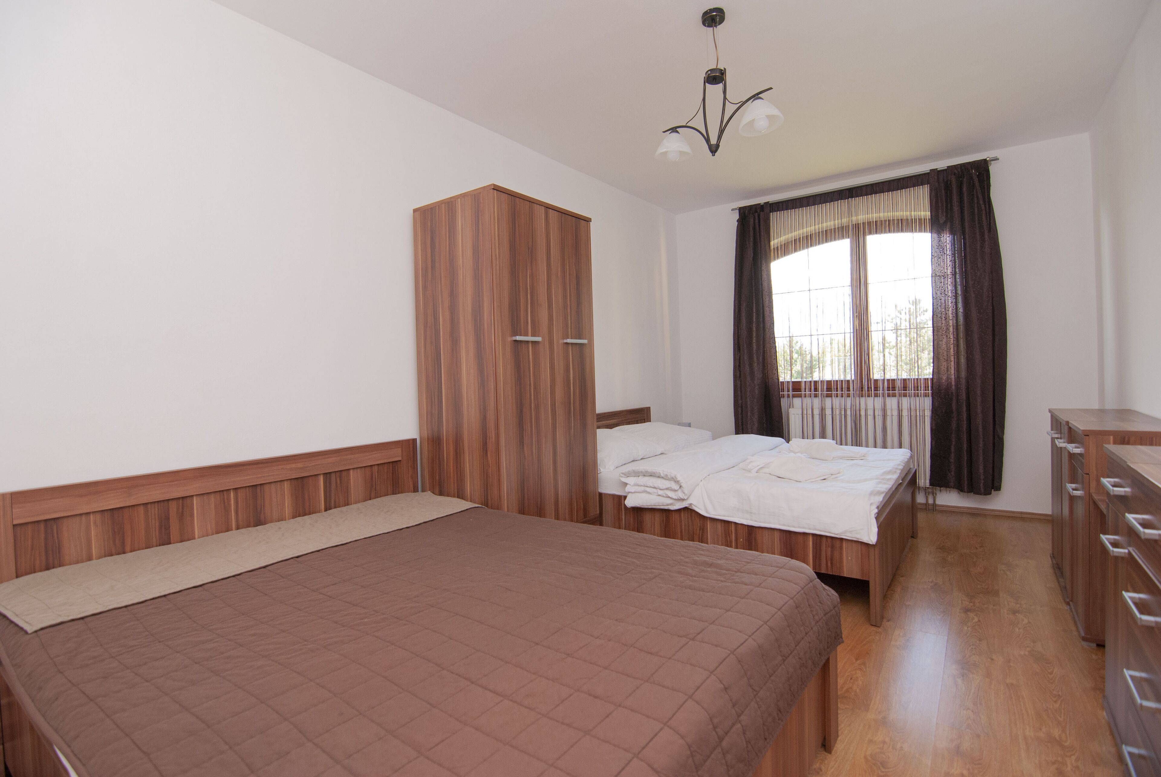 A bedroom with a large bed, a wardrobe, a dresser, and a window with curtains.