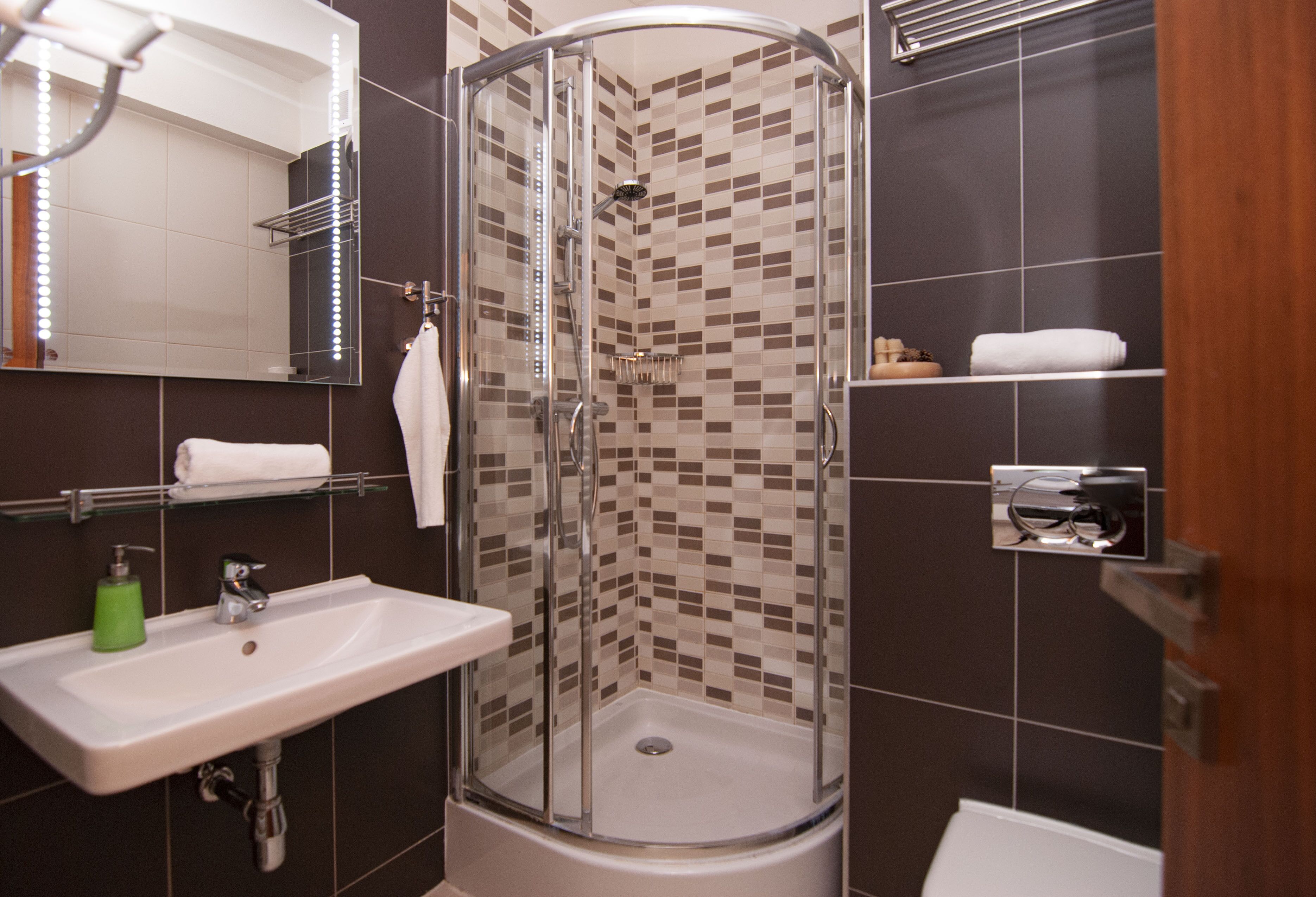 A modern bathroom with a glass-enclosed shower, a sink with a soap dispenser, and a mirror with lights.