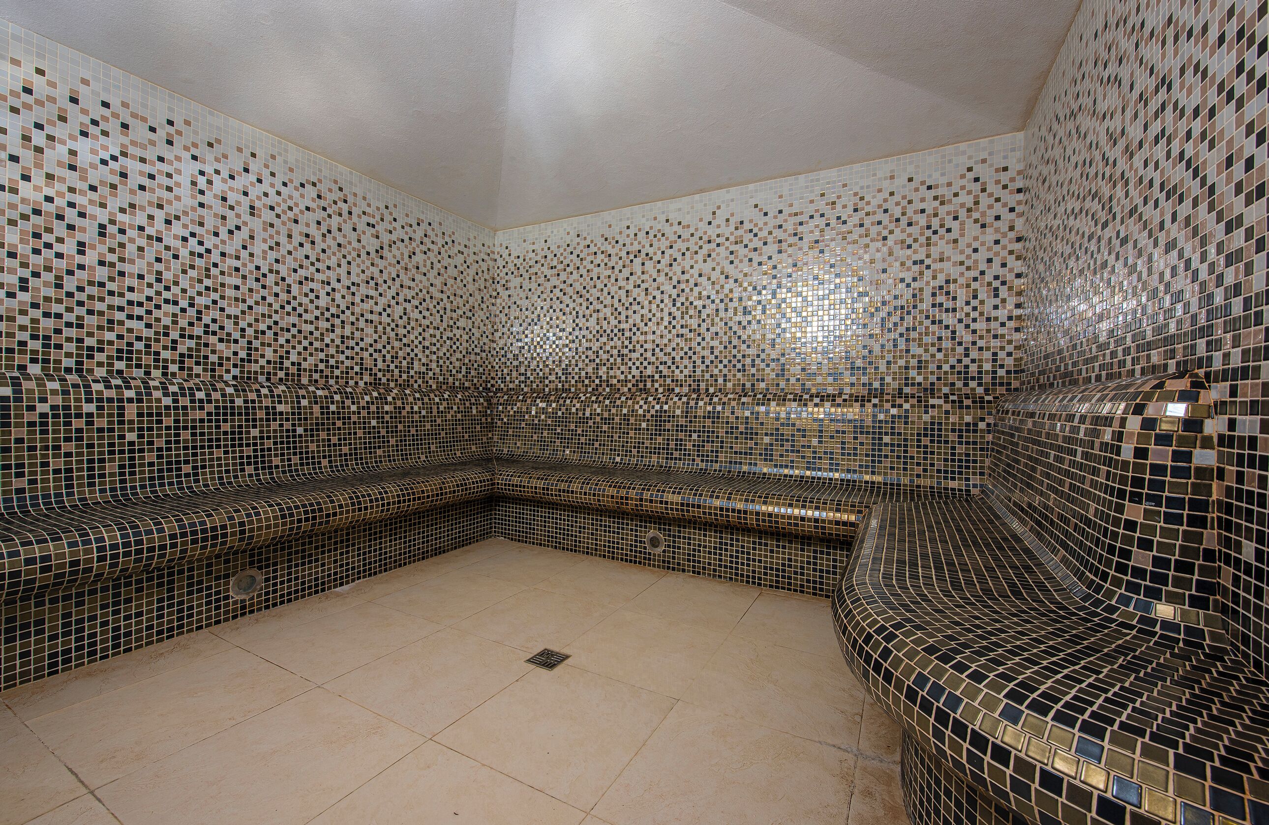 Un cuarto de spa con paredes de mosaicos y un banco curvo.