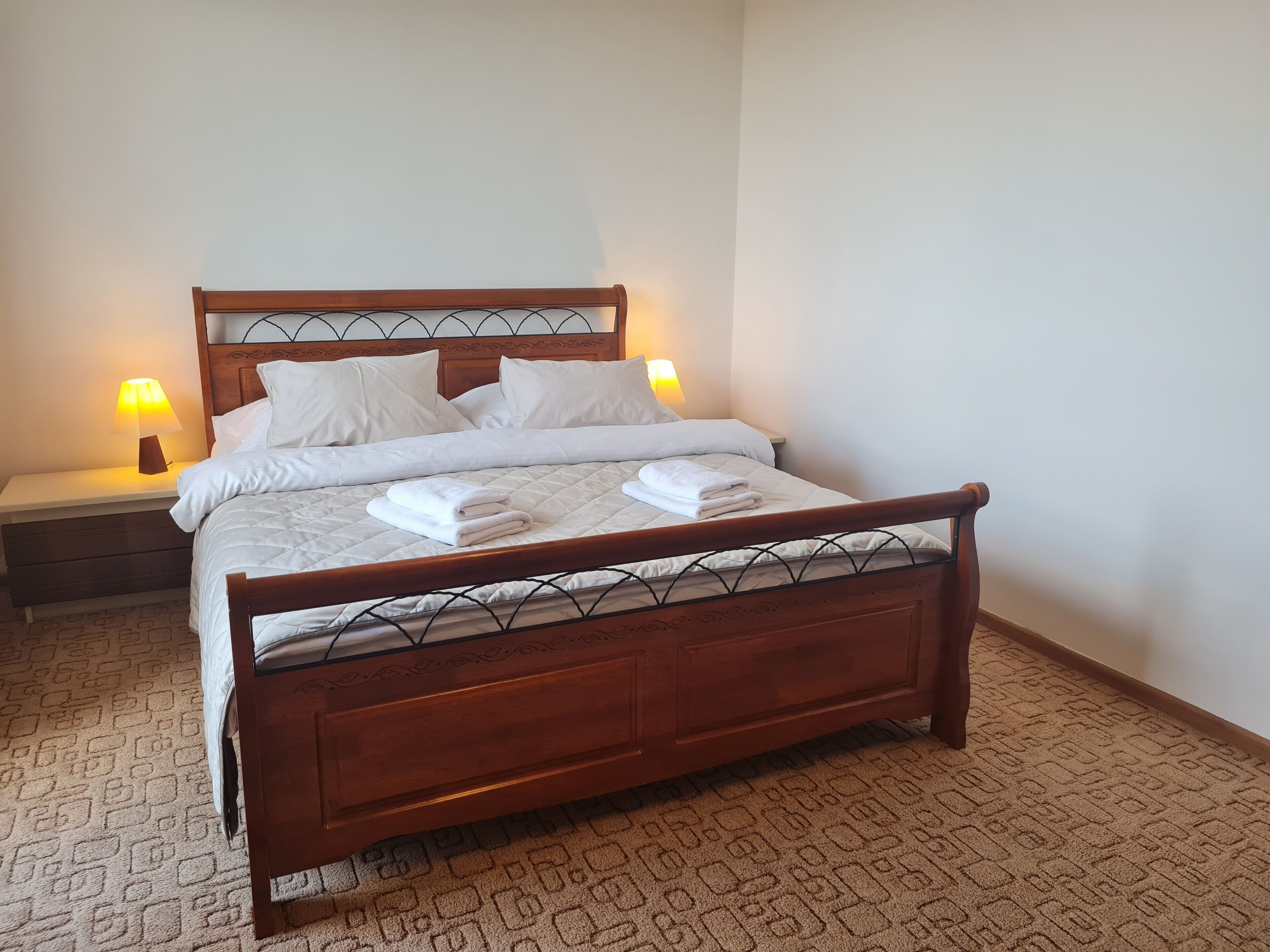 Un lit bien fait, avec du linge de lit blanc et deux oreillers, une tête de lit en bois et deux lampes de chevet.
