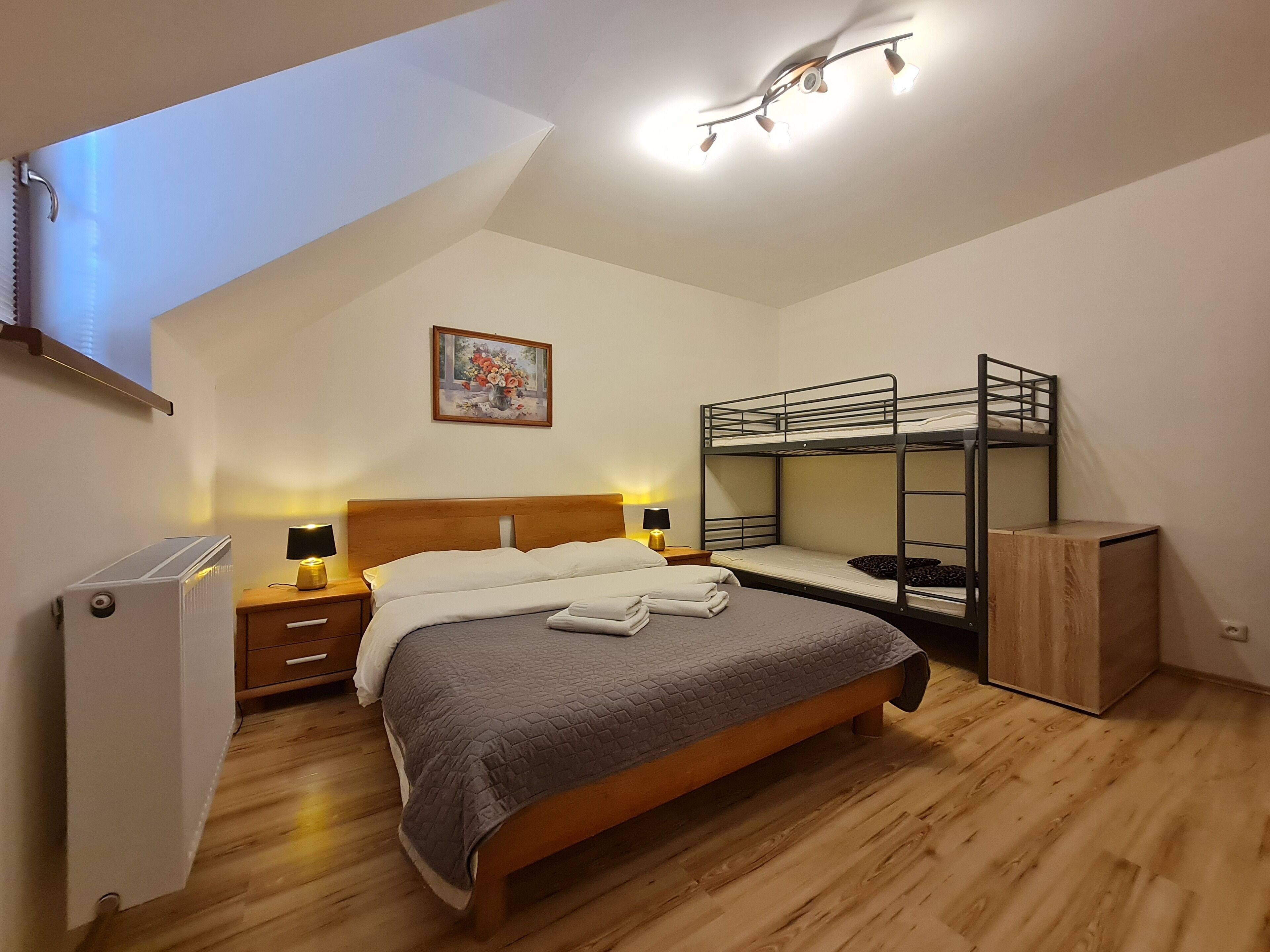 Un dormitorio con una cama nido, un escritorio, una silla, una lámpara y un cuadro en la pared.