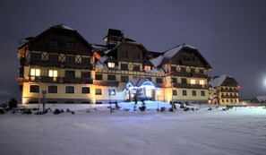 A large, multi-story building with a traditional architectural style, featuring a snow-covered ground and illuminated windows. - Apartmány Sileas (Velka Lomnica)