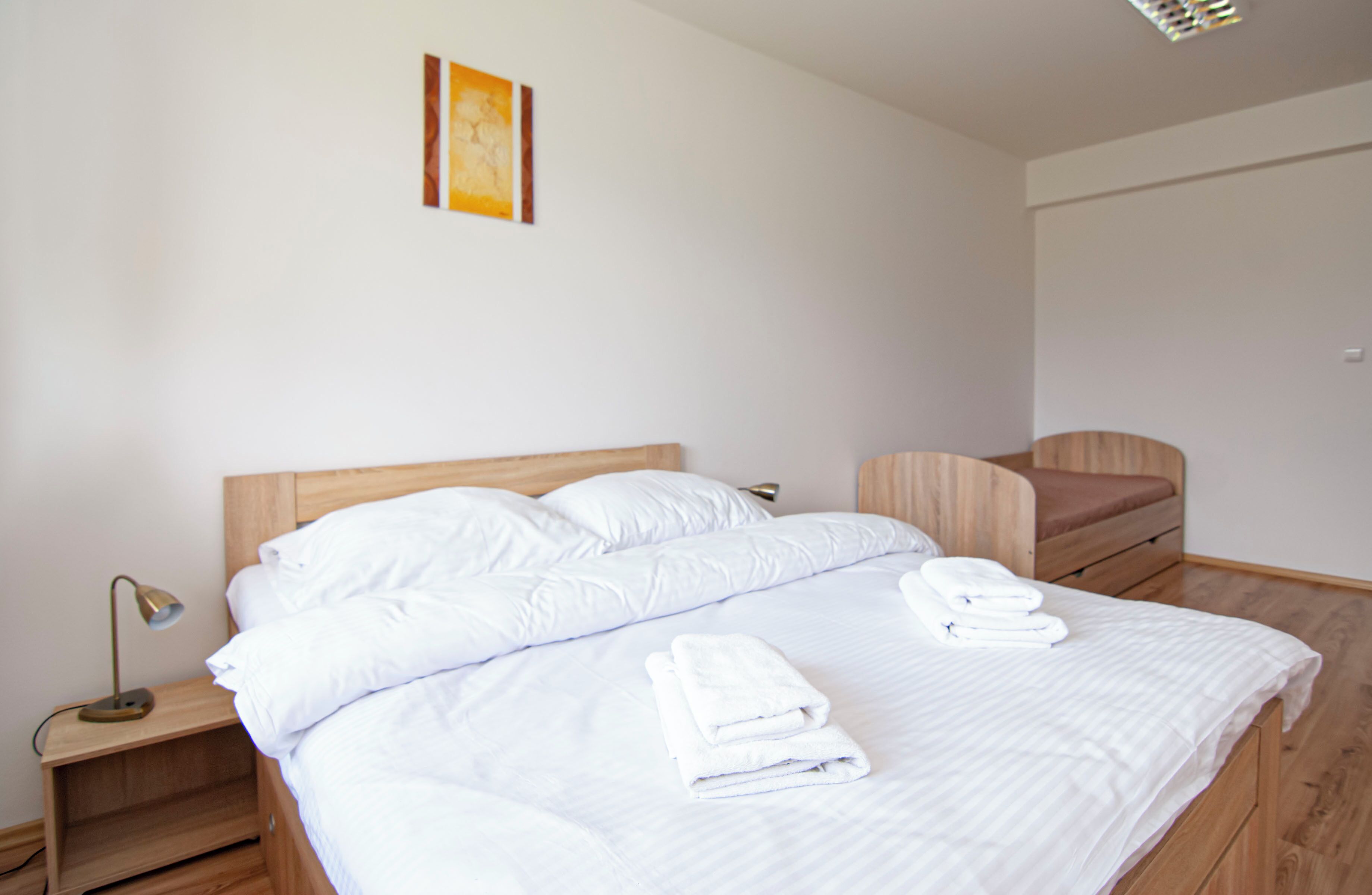 A neatly made bed with white linens and towels, a bedside lamp, and a wooden nightstand.