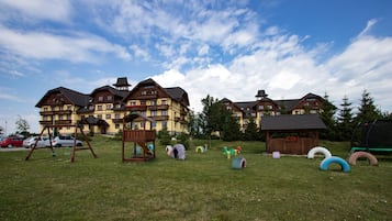 A large hotel with multiple buildings, a grassy area with playground equipment, and a clear sky.