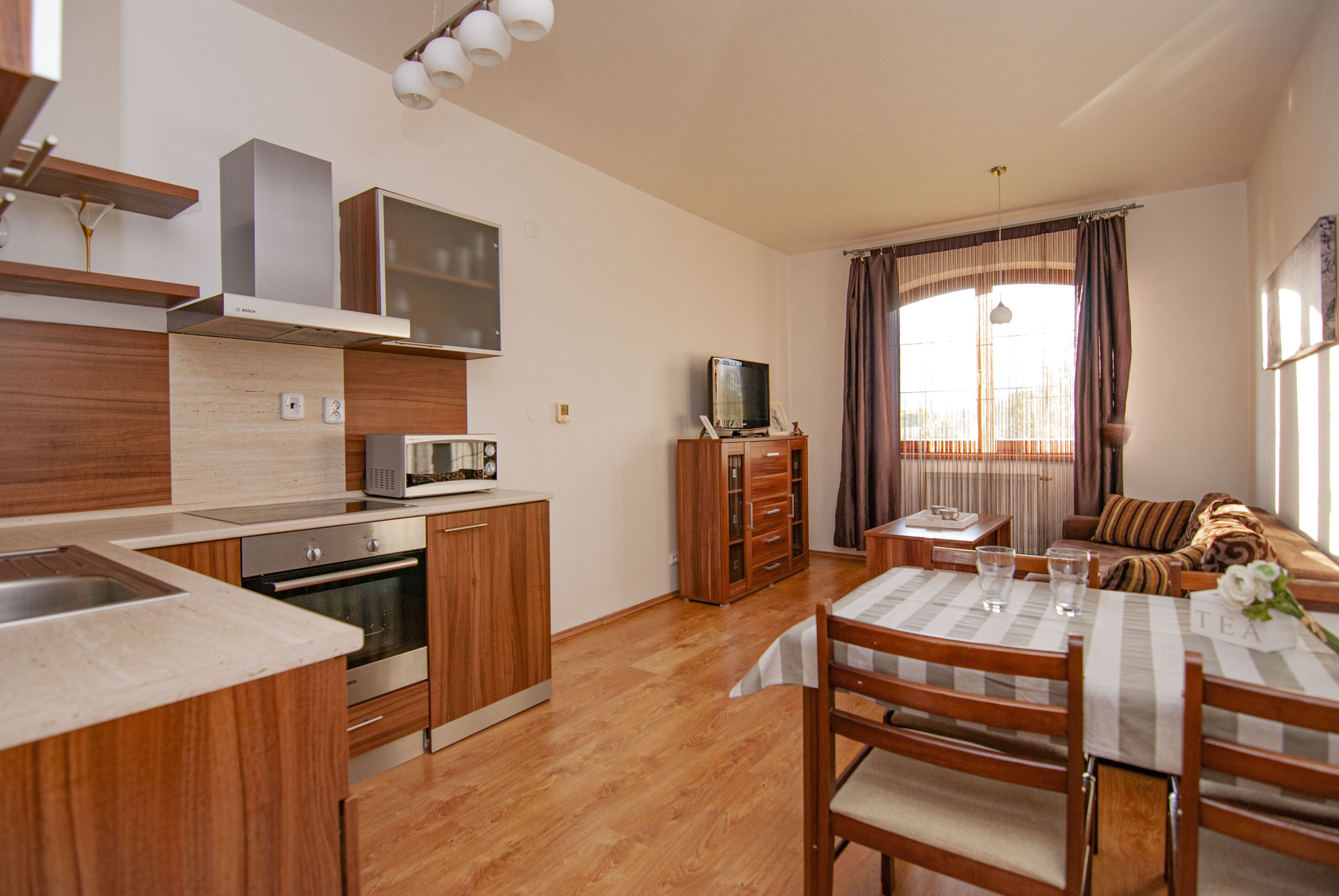 Cocina compacta con electrodomésticos modernos, comedor con mesa y sillas, y sala de estar acogedora con sofá y cortinas.