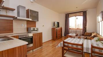 Una cucina compatta con elettrodomestici moderni, una zona pranzo con tavolo e sedie, e un angolo soggiorno accogliente con divano e tende.