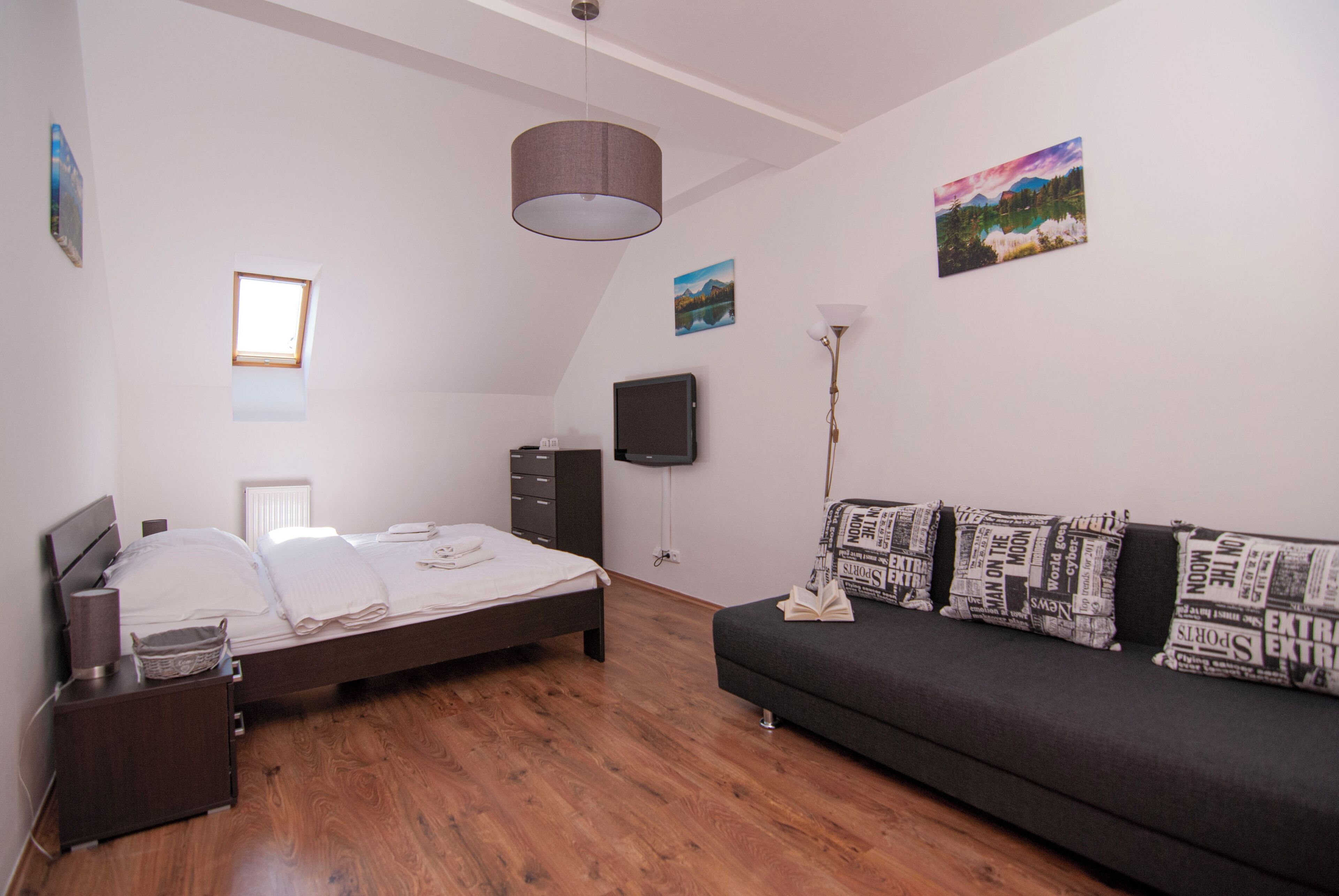 Un dormitorio con cama, cómoda, mesita de noche, sofá, lámpara y dos cuadros en la pared.