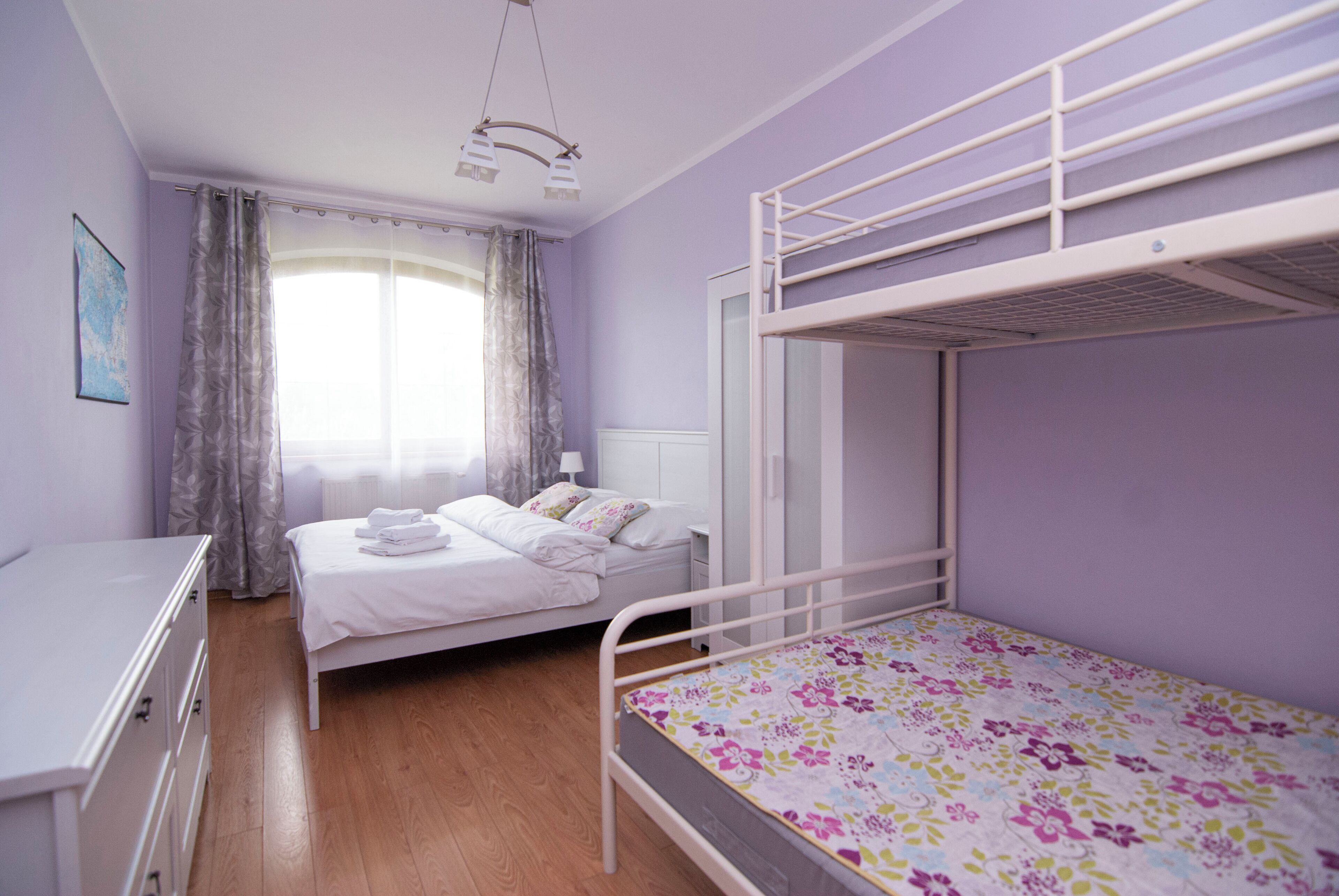 Un dormitorio con una cama litera, una cama individual, un aparador y una ventana con cortinas.