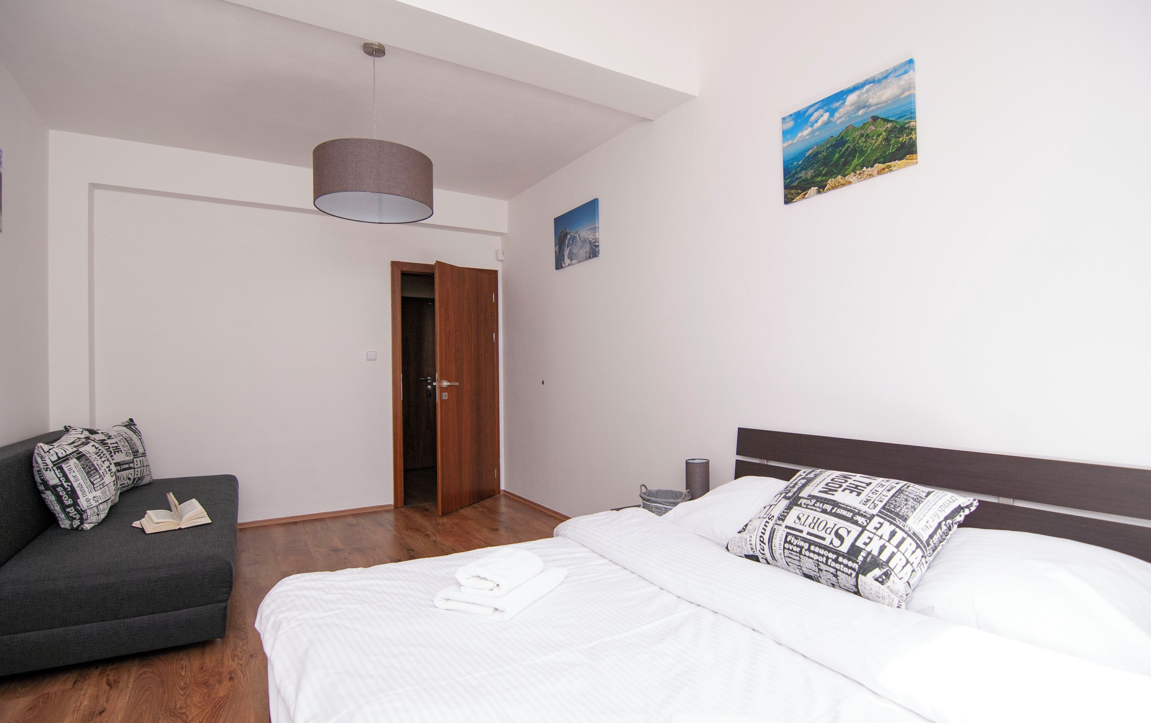 A hotel room with a bed, a sofa, a wooden door, a painting, and a ceiling light.