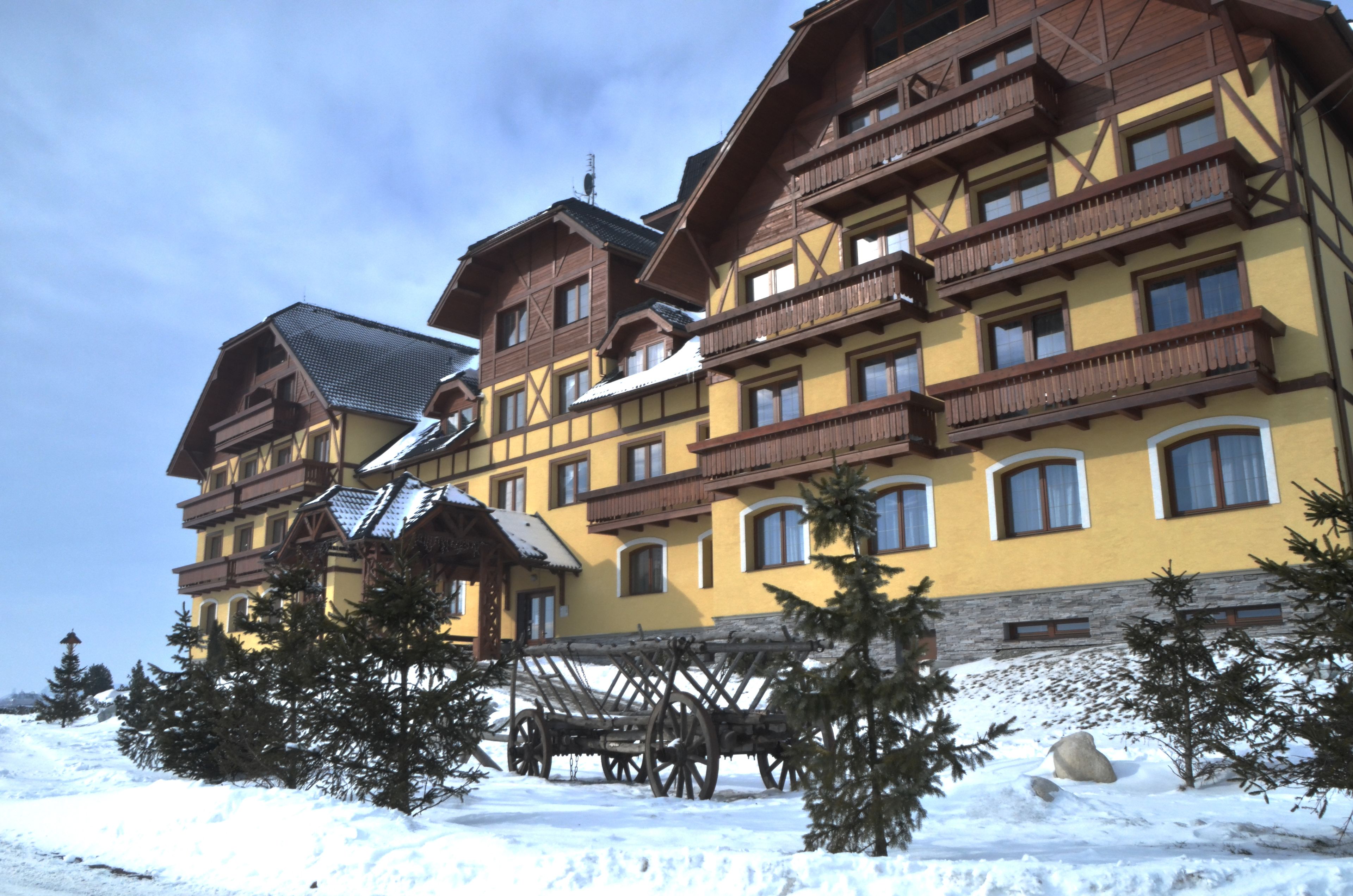 A multi-story hotel with a traditional Alpine architectural style, featuring wooden balconies and a snow-covered ground.