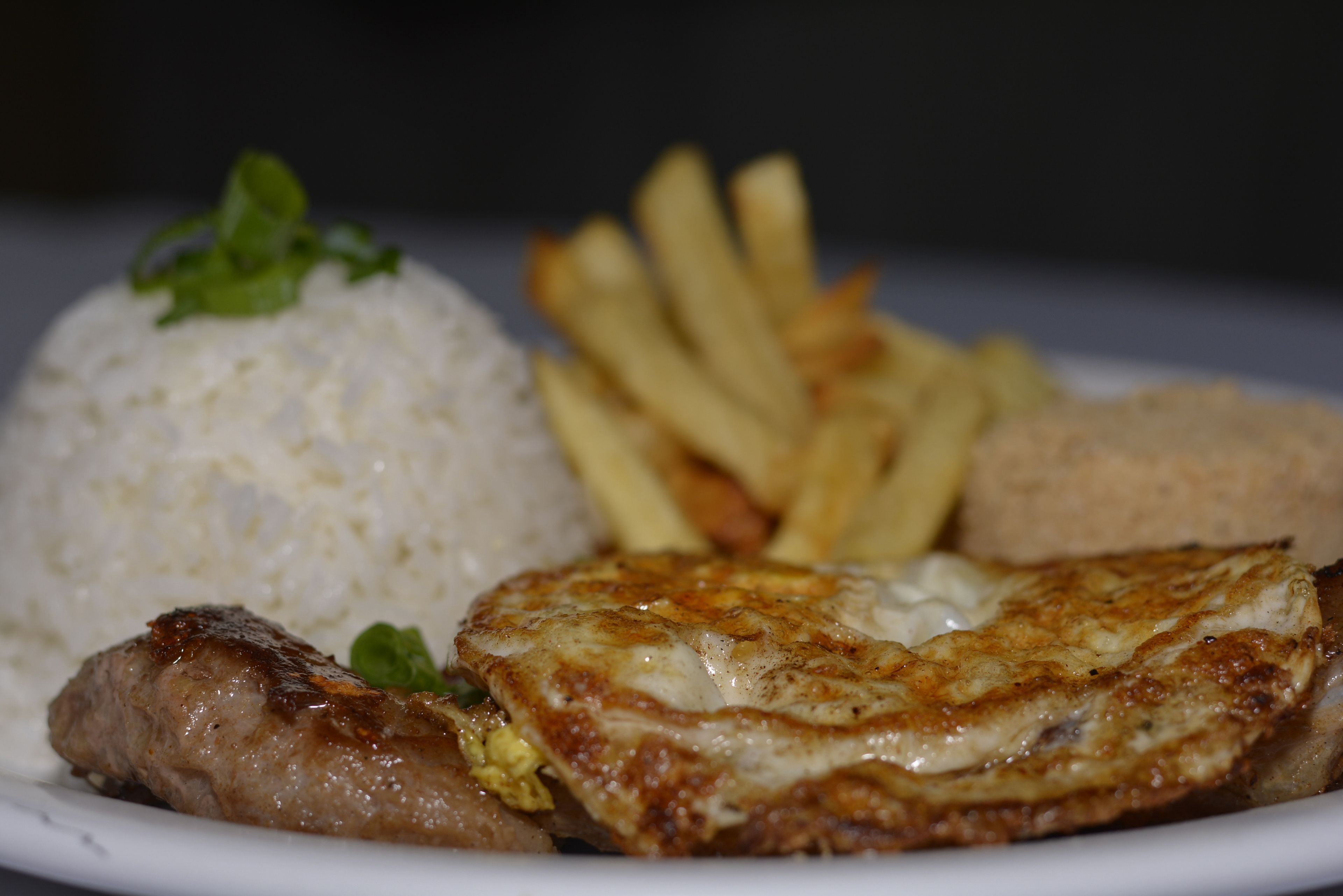 Une assiette contenant du riz, des frites, une galette de viande et un œuf frit.