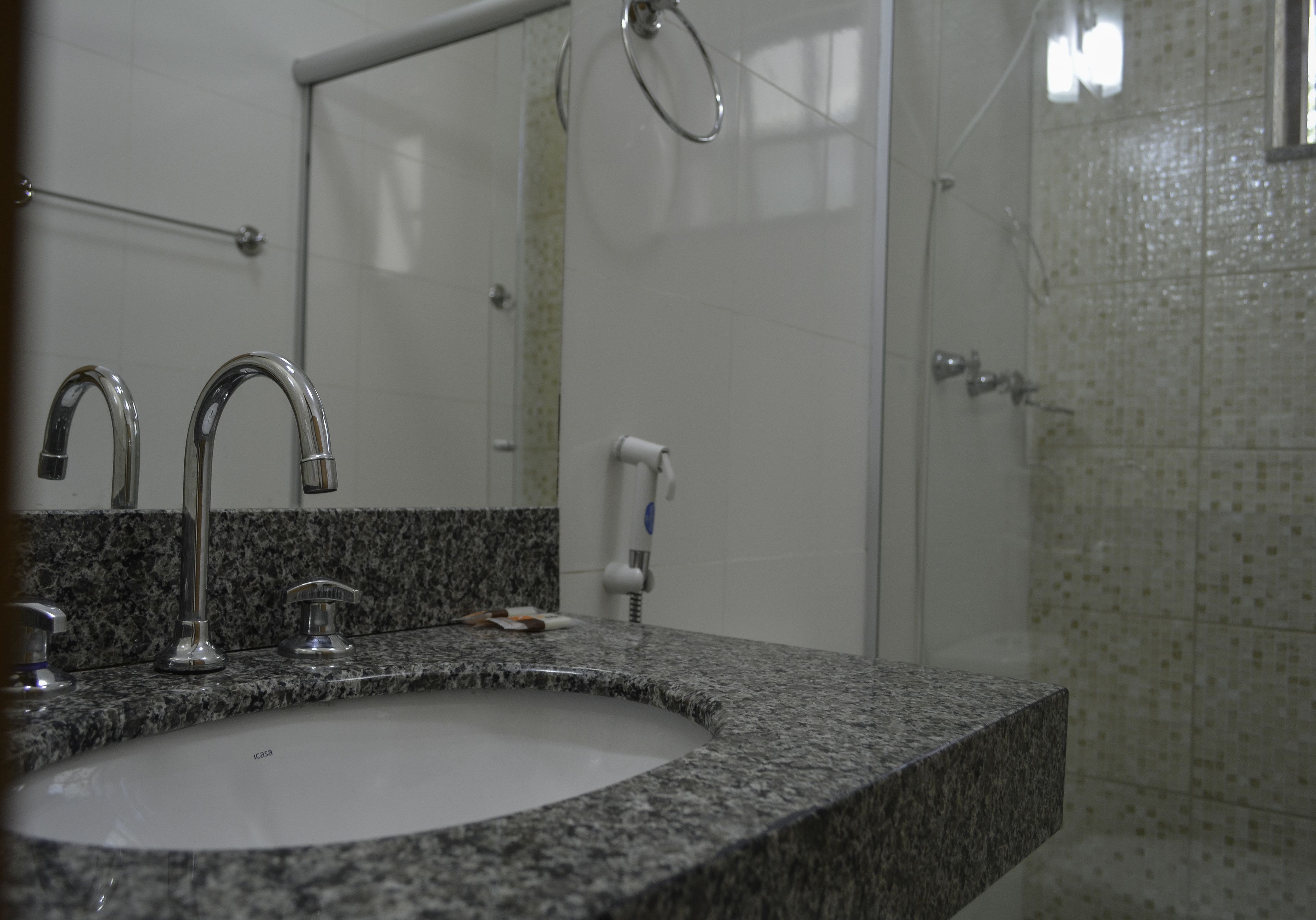 Un baño con encimera de granito, lavamanos, espejo y zona de ducha.