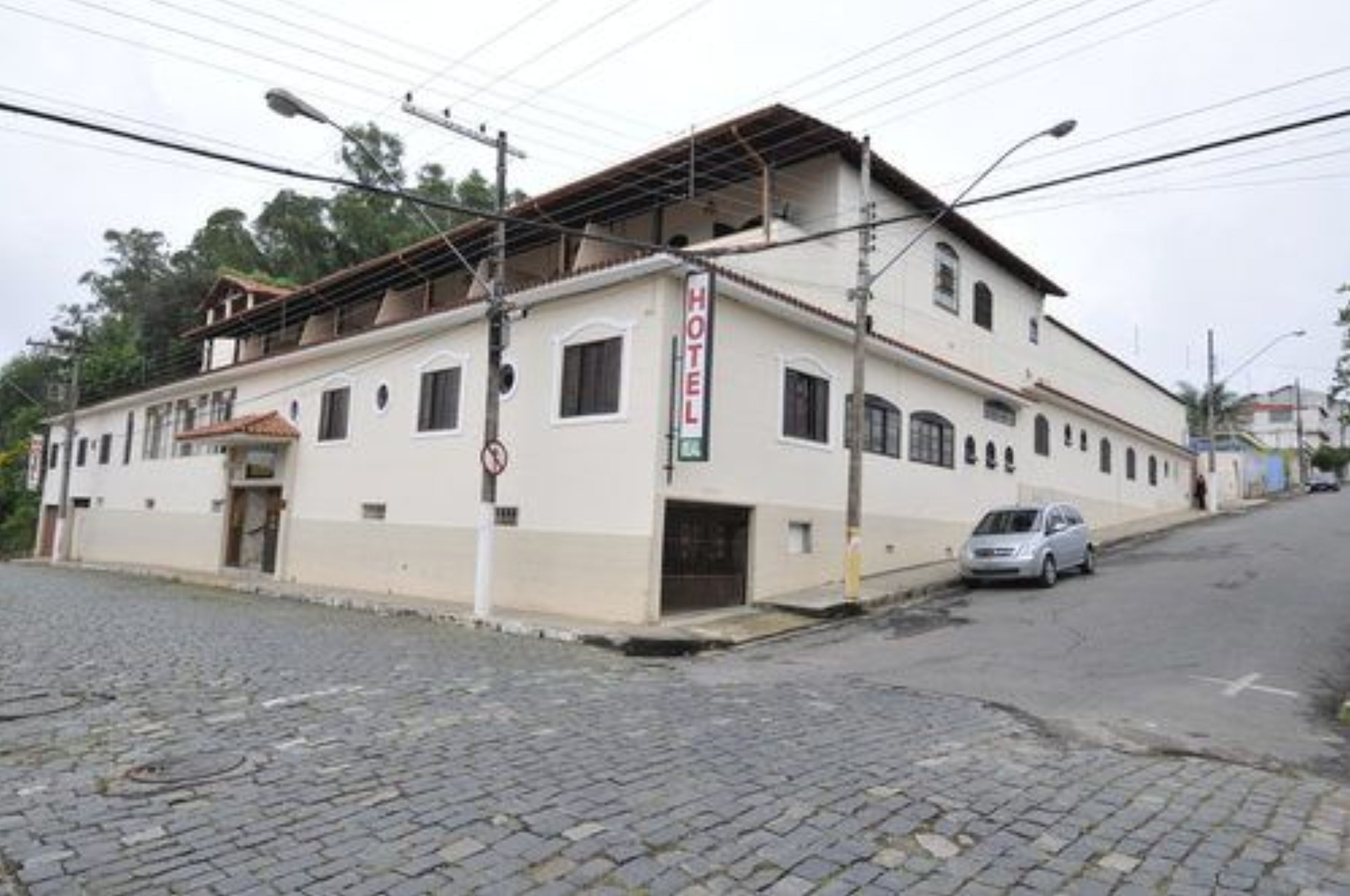 Un edificio de dos pisos con un letrero que indica que es un hotel. El edificio tiene un techo plano, varias ventanas y una calle pavimentada en su parte frontal.