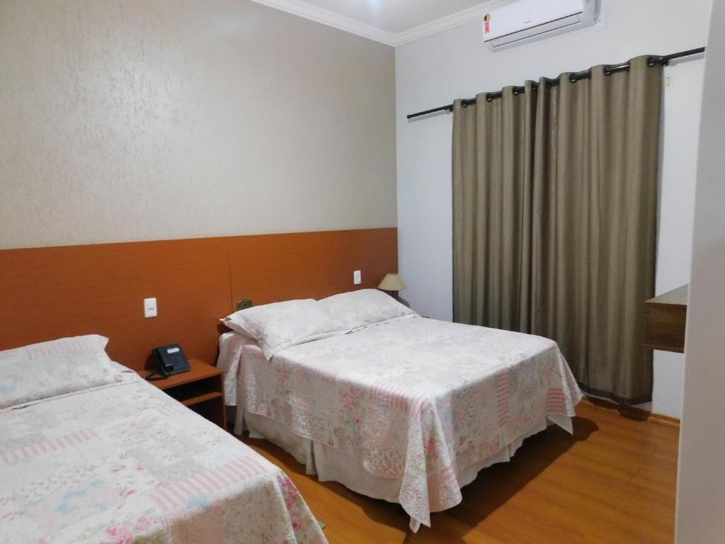 Een hotelkamer met twee bedden, een houten vloer, een wandairconditioner en een gordijn.
