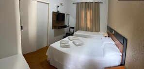 Habitación de hotel con dos camas, un televisor montado en un panel de madera, una silla y una ventana con cortinas.