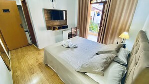 Een hotelkamer met een bed, een aan de muur bevestigde televisie, een deur met een nummer en een raam met gordijnen.