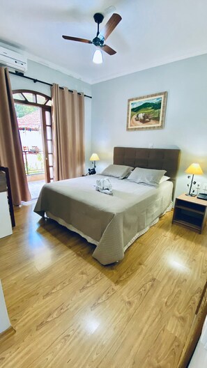 Un dormitorio con cama, ventilador de techo, un cuadro y ventana con cortinas.