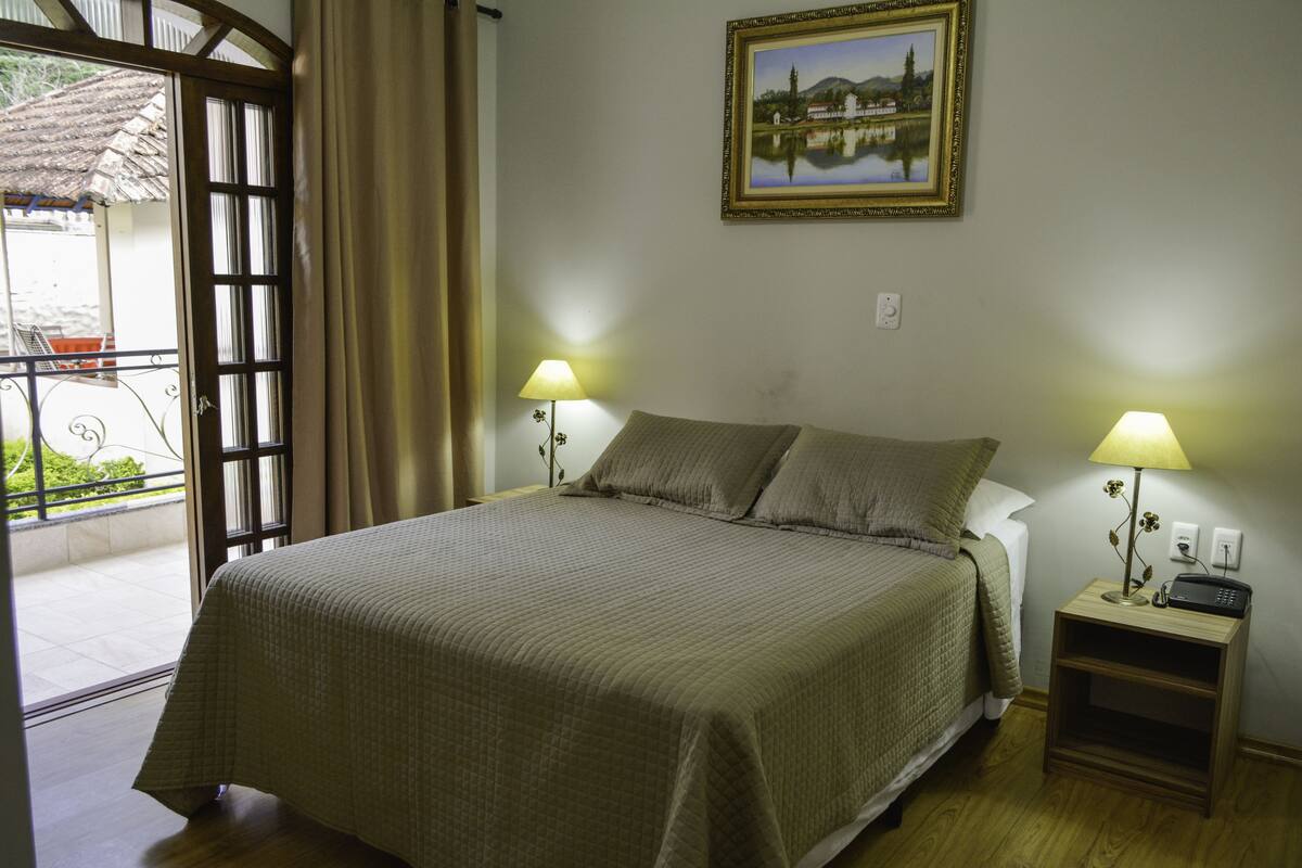 Un dormitorio con una cama, dos lámparas de noche, una mesita de noche con un radio y un cuadro en la pared.