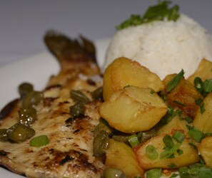 Un plato con pollo a la parrilla, patatas asadas y arroz como guarnición.