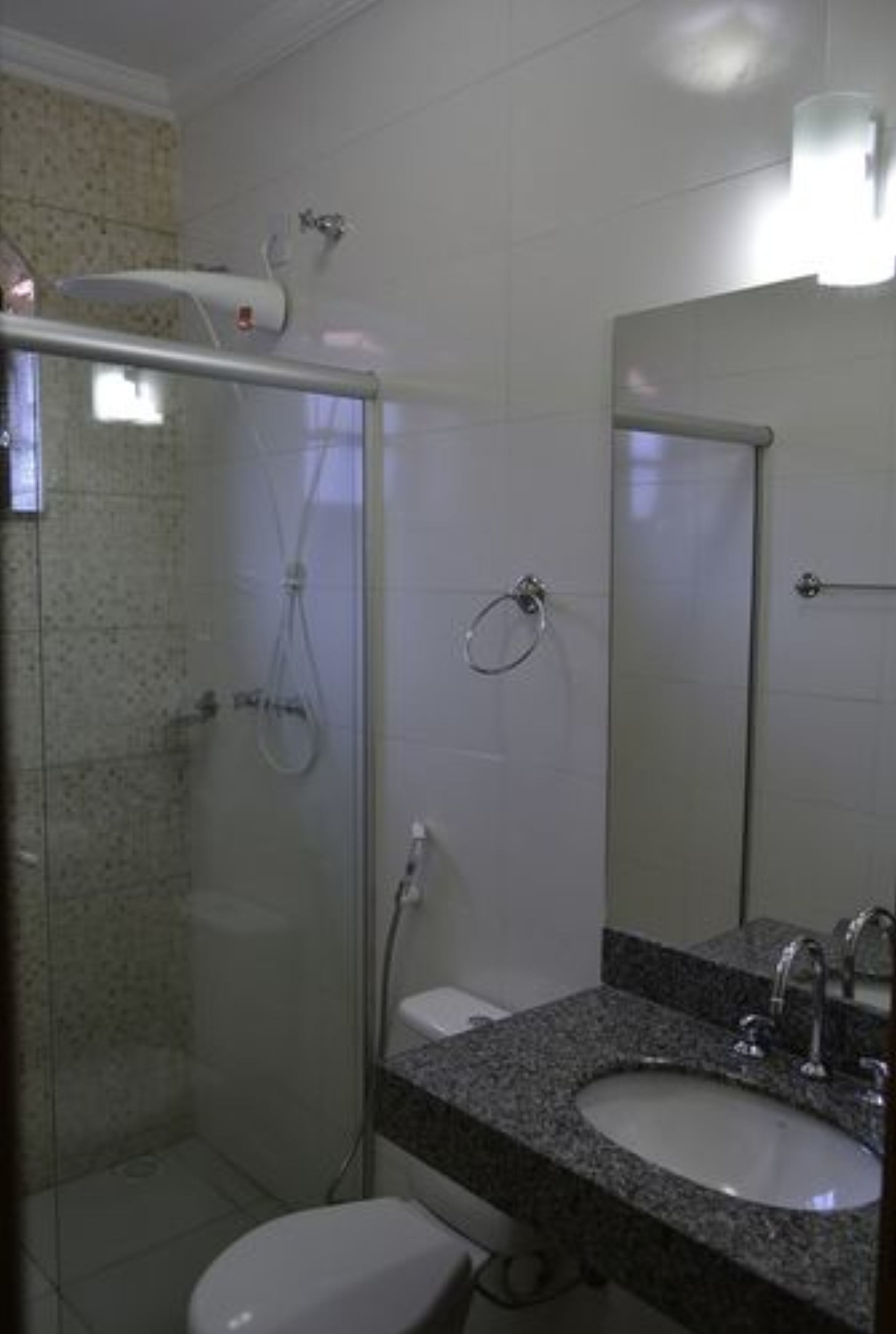 Uma casa de banho com cabine de chuveiro em vidro, uma pia com bancada de granito e um espelho sobre a pia.