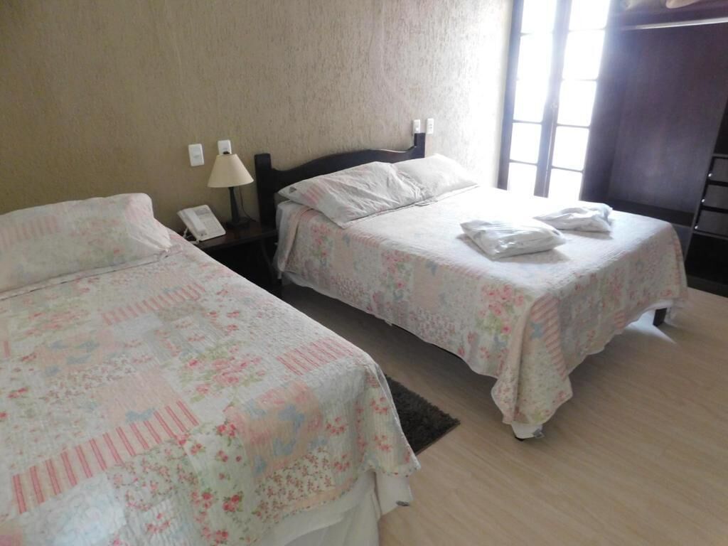 Two single beds with floral bedding, a bedside lamp, a phone, and a window with curtains.