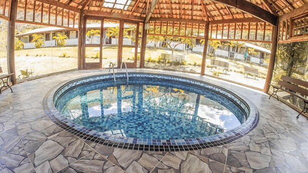Una piscina circular con mosaicos y suelo de piedra, rodeada por una pérgola de madera con paneles de vidrio.