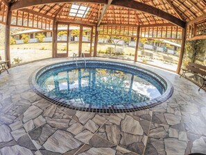 A circular pool with mosaic tiles and a stone floor, surrounded by a wooden pergola with glass panels. - Pousada Campestre São Lourenço (Sao Lourenco)