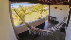 Una hamaca en un balcón con vistas a un paisaje verde y una estructura de techo de paja.