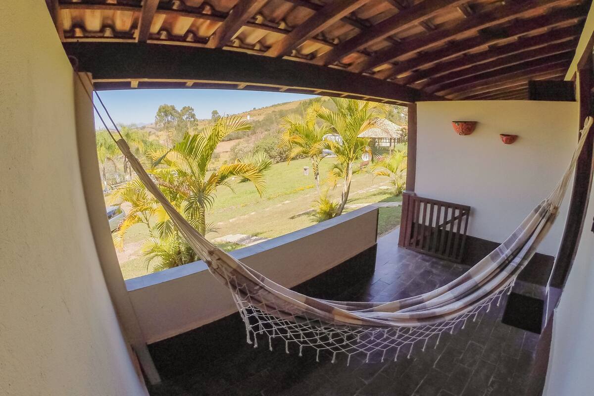 Una hamaca en un balcón con vistas a un paisaje verde y una estructura de techo de paja.