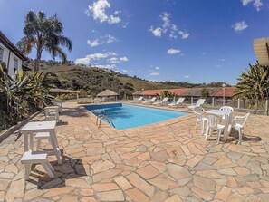 A swimming pool with lounge chairs and tables, surrounded by stone tiles and palm trees. - Pousada Campestre São Lourenço (Sao Lourenco)