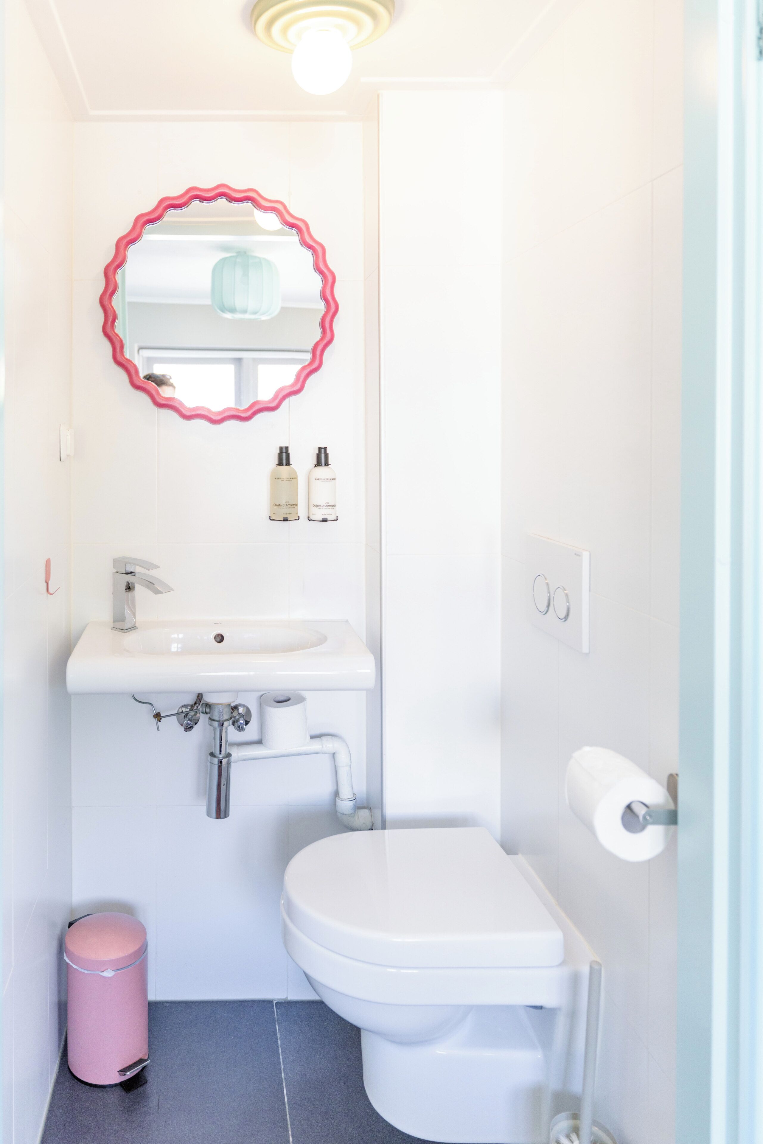 Un baño con lavamanos blanco, inodoro y un bote de basura rosa.
